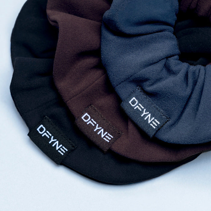 Close-up of 3 fabric scrunchies with DRYNE woven labels in black, navy, and dark brown