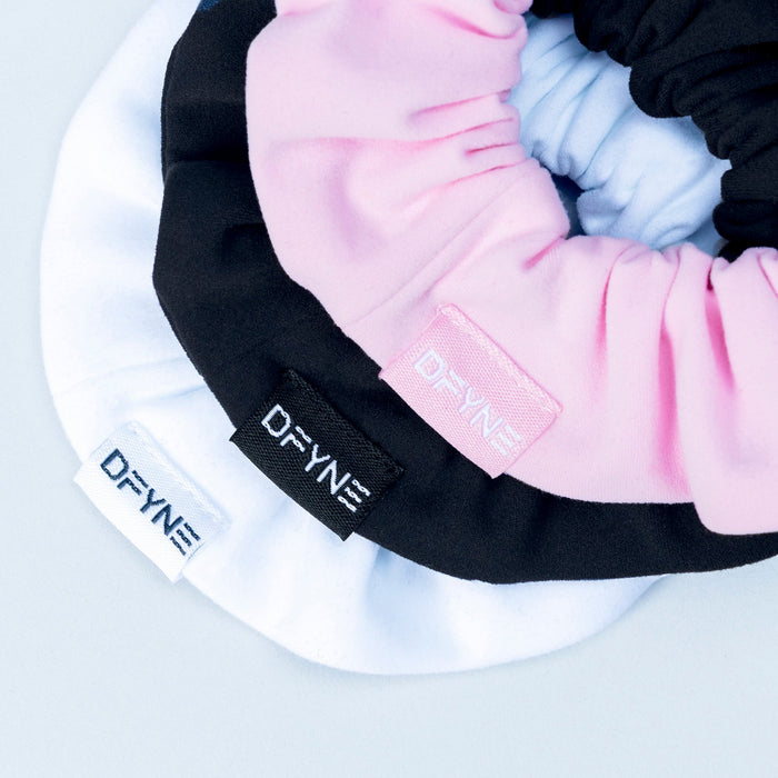 Close-up of black and pink satin scrunchies with embroidered logo bands