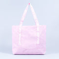 Light pink tote bag with wide handles and vertical logo tape on each side.