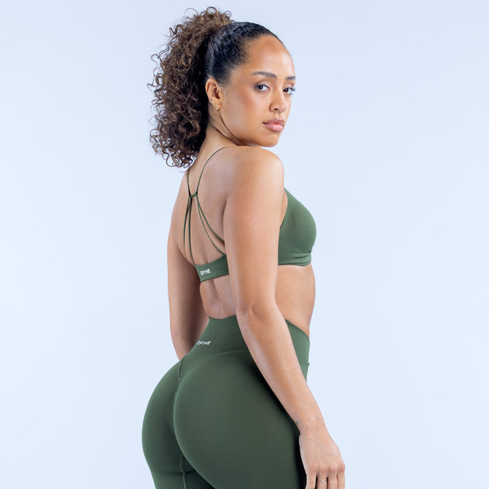 Green twist-front sports bra with thin back straps and DPYNE logo patch.